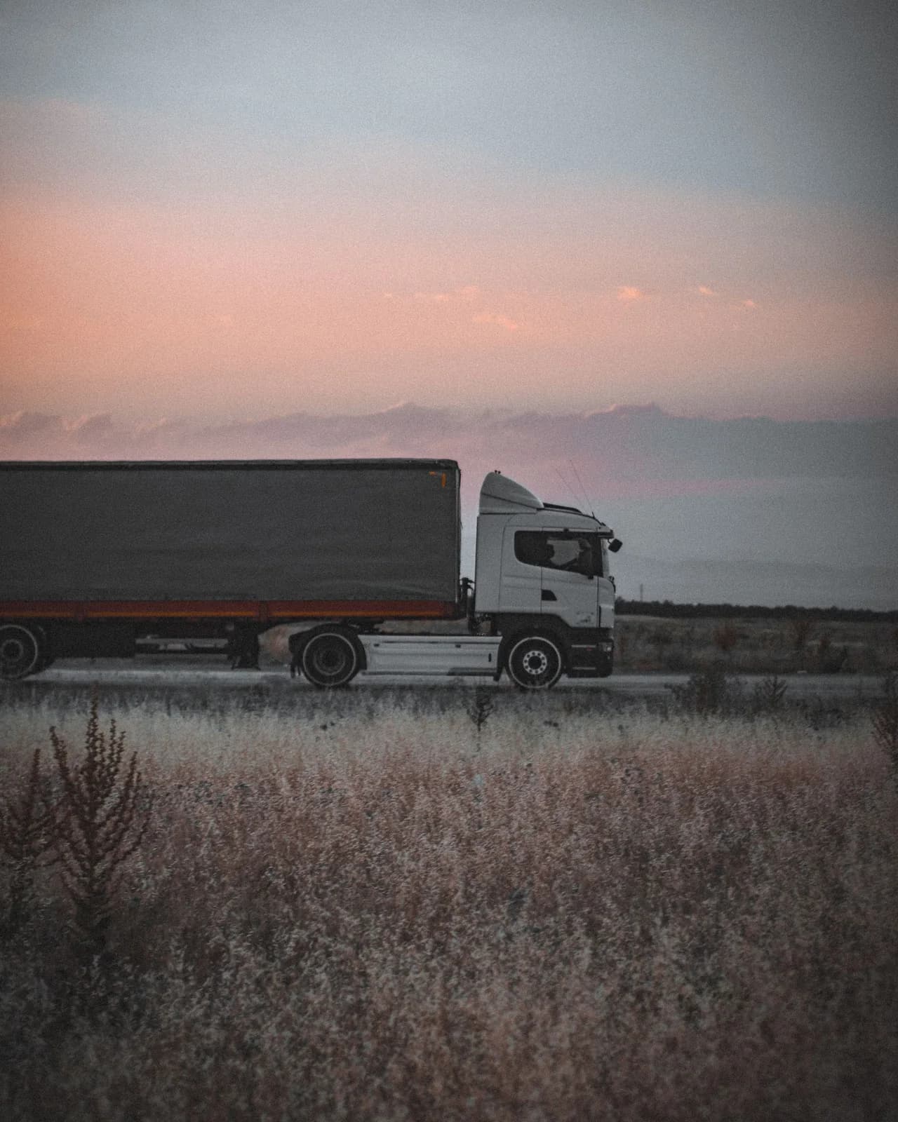 Freight truck travelling on a road at sunset.