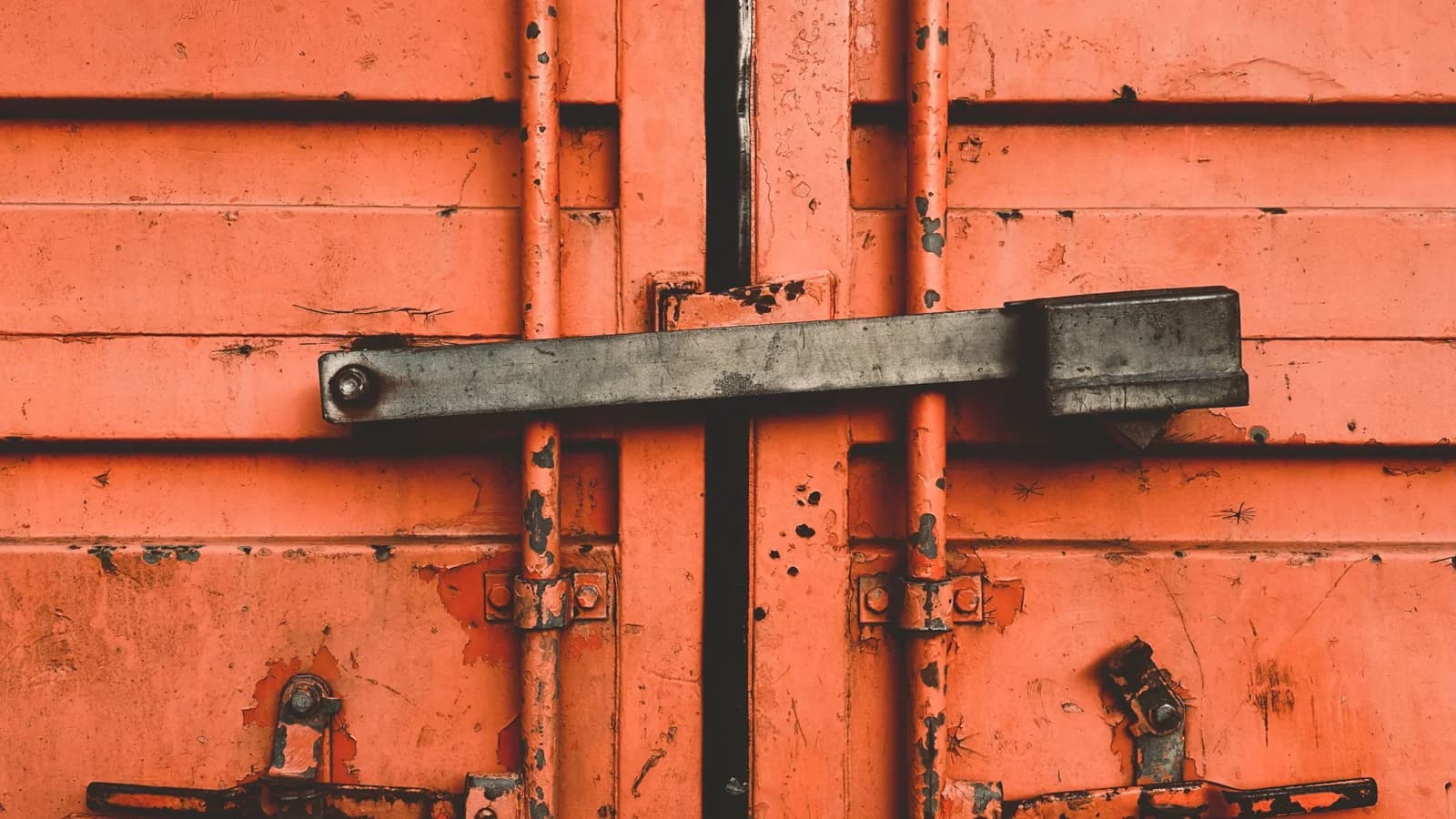 Close-up of a weathered shipping-container door, latch and painted surface.