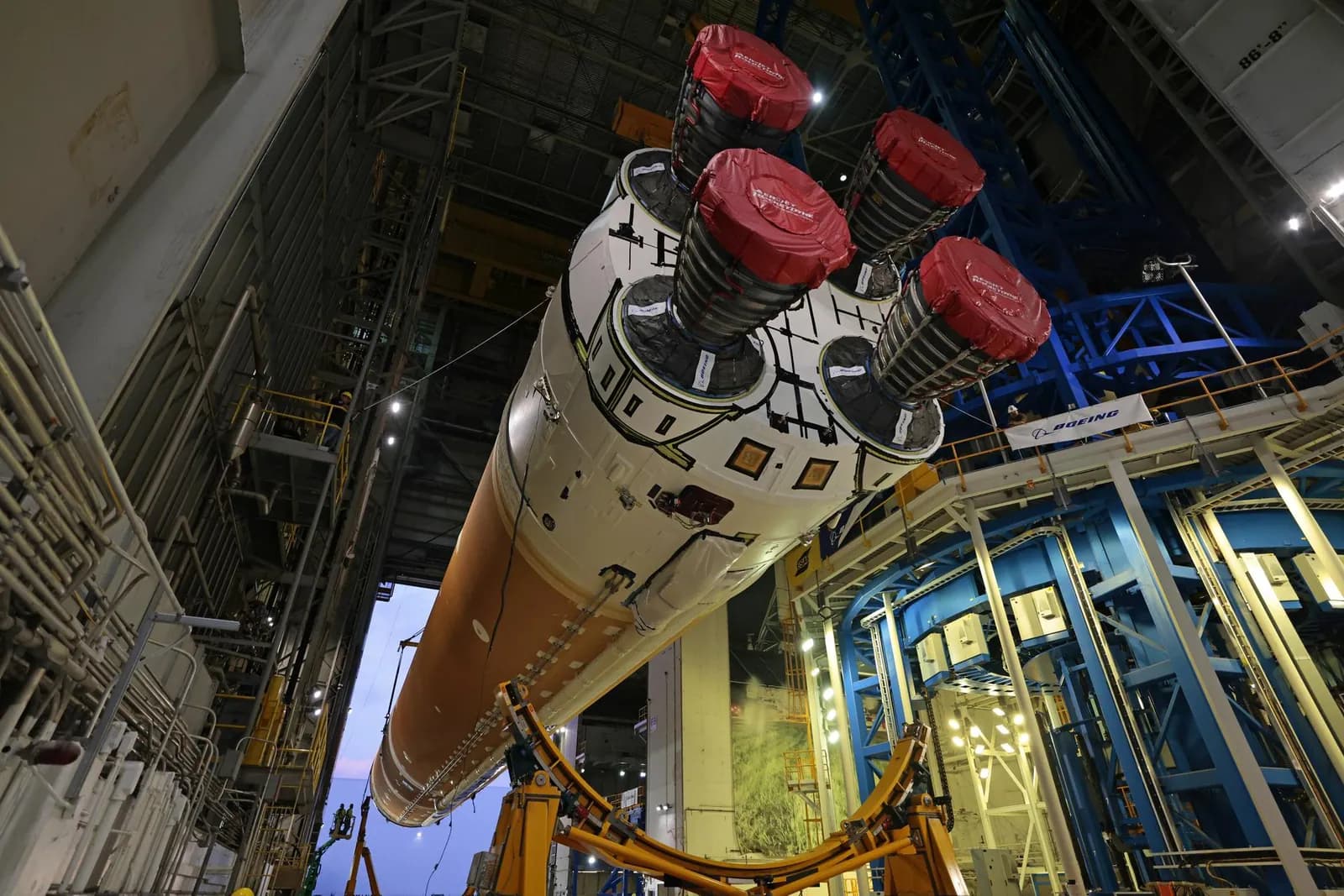 A rocket core stage with four engines is lifted inside a tall assembly building.